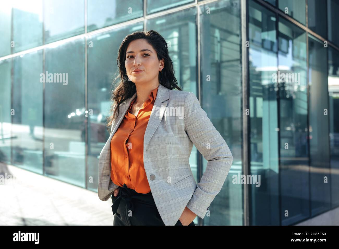Female white collar worker looking at the camera while standing in front of a high rise office building in the city. Self-confident businesswoman stan Stock Photo