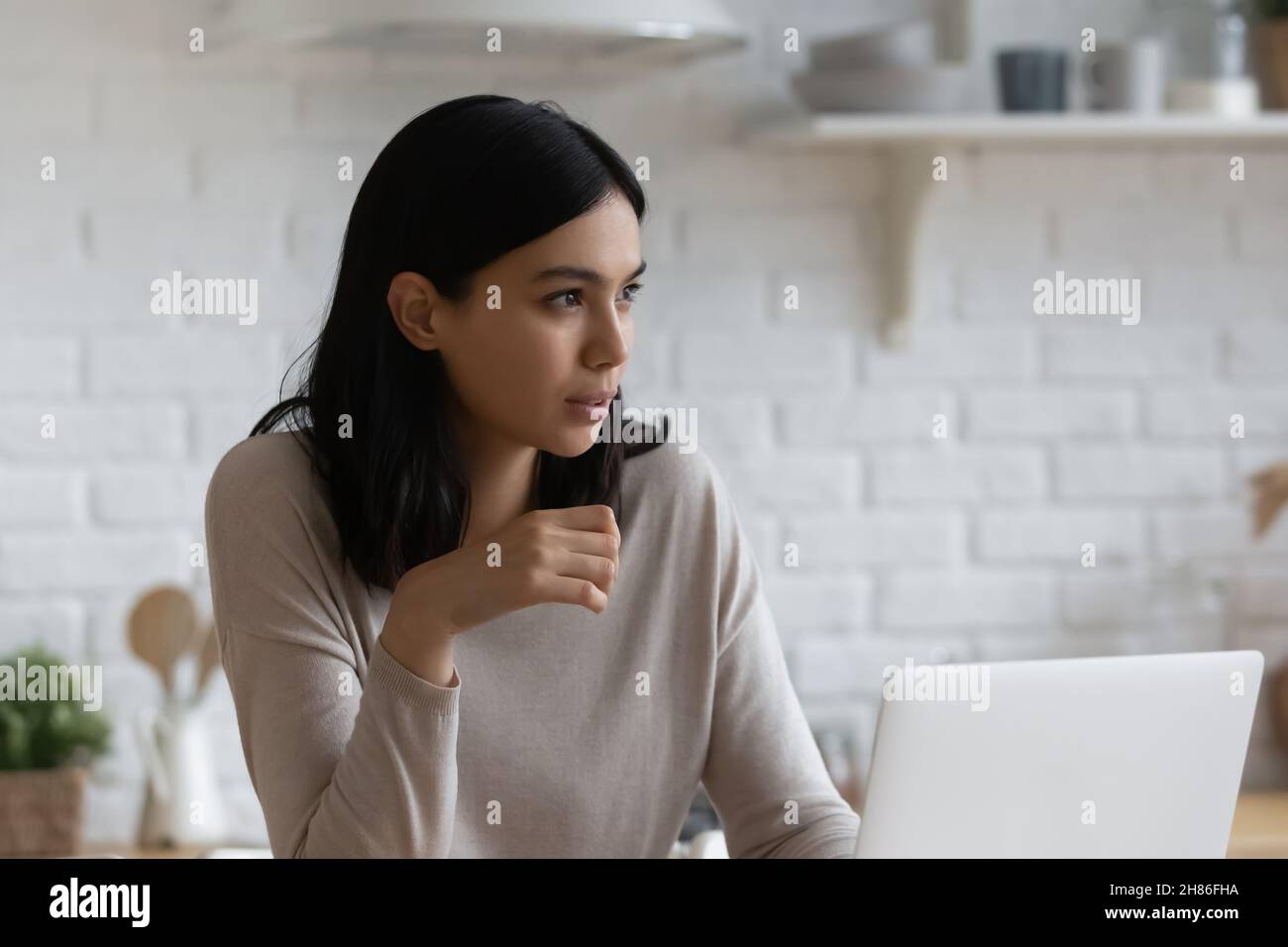 Young thoughtful Asian woman sit indoor with laptop Stock Photo
