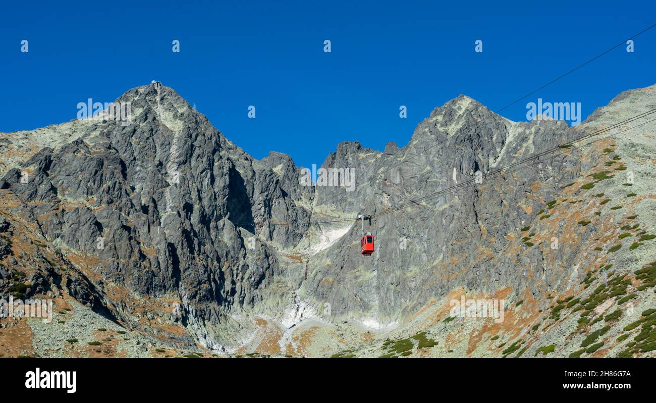 A red cable car on its way from Skalnate pleso to Lomnicky peak. Red gondola moving up to Lomnica peak in High Tatras Mountains. Slovakia. Stock Photo