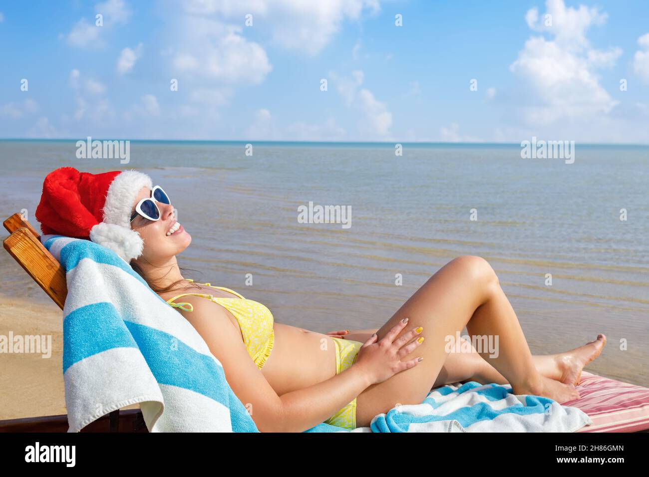 beautiful young woman in santa hat and sunglasses relaxing on sun lounger Stock Photo