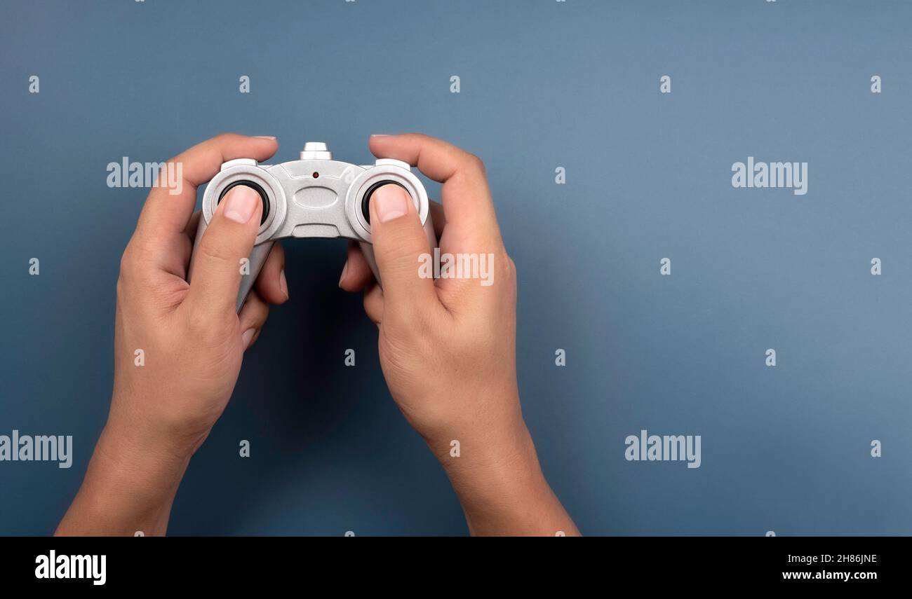 Hand holding and using silver retro style radio remote control for a toy isolated on blue background with copy space, top view. Game controller  joyst Stock Photo
