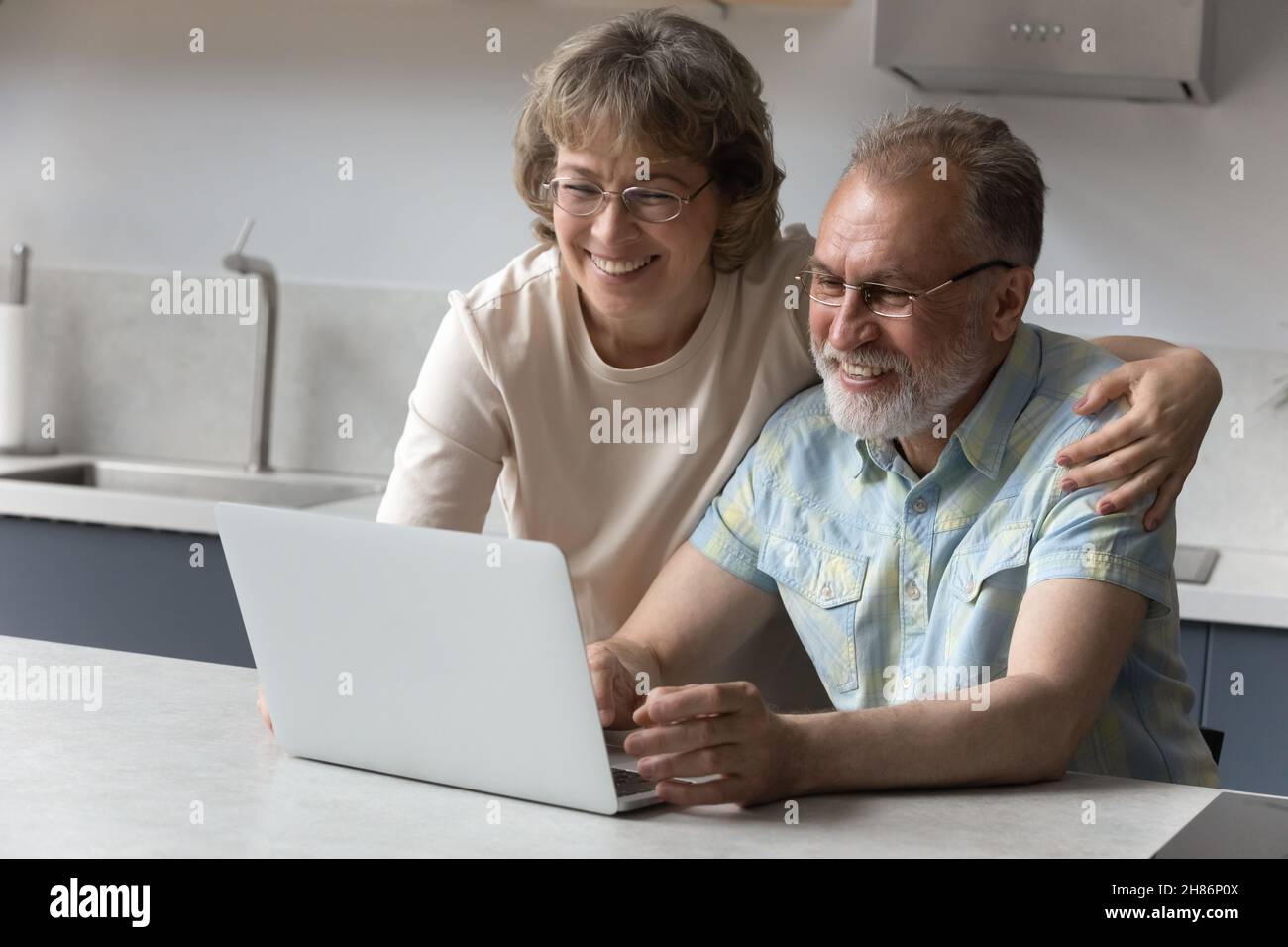 Happy old couple using laptop in kitchen, making video call Stock Photo