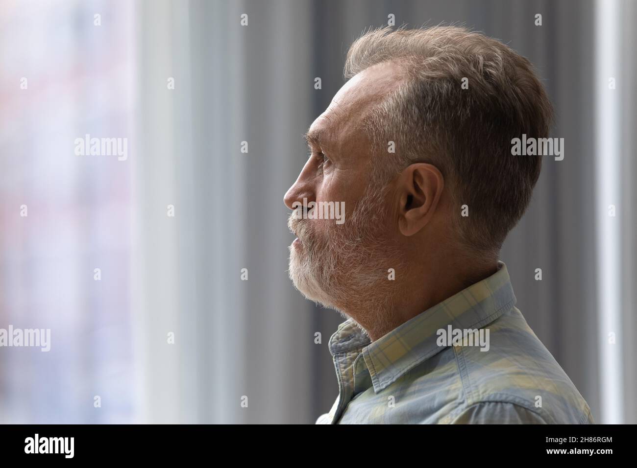 Sad thoughtful older 60s man looking out of window Stock Photo