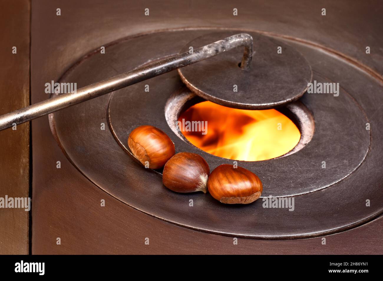Close-up of three chestnuts over a fire in a wood stove.The photo represents something typical of the autumn season and is taken in horizontal format. Stock Photo