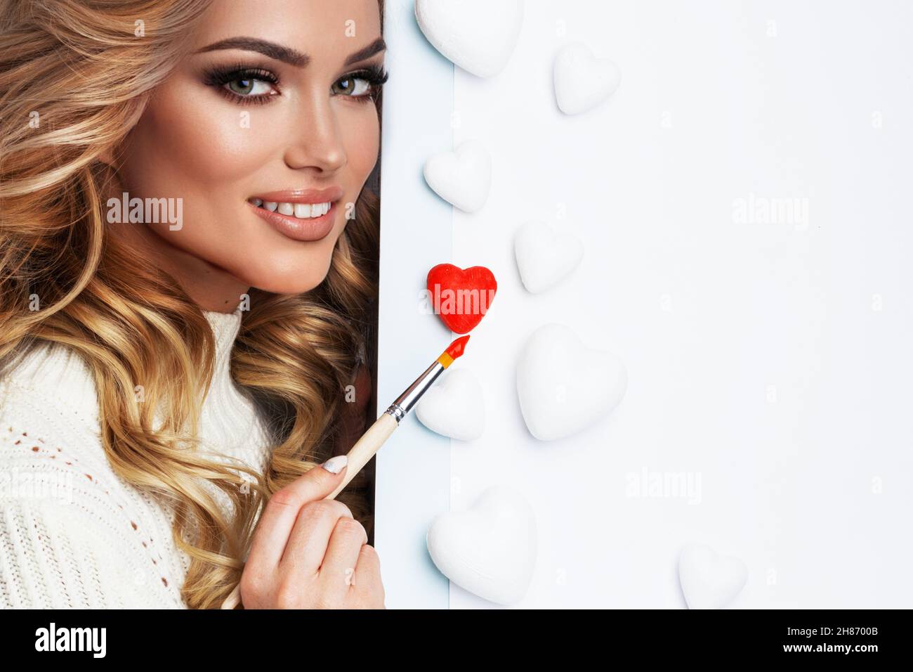 Beautiful young woman painting hearts with red paint Valentine day love concept Stock Photo