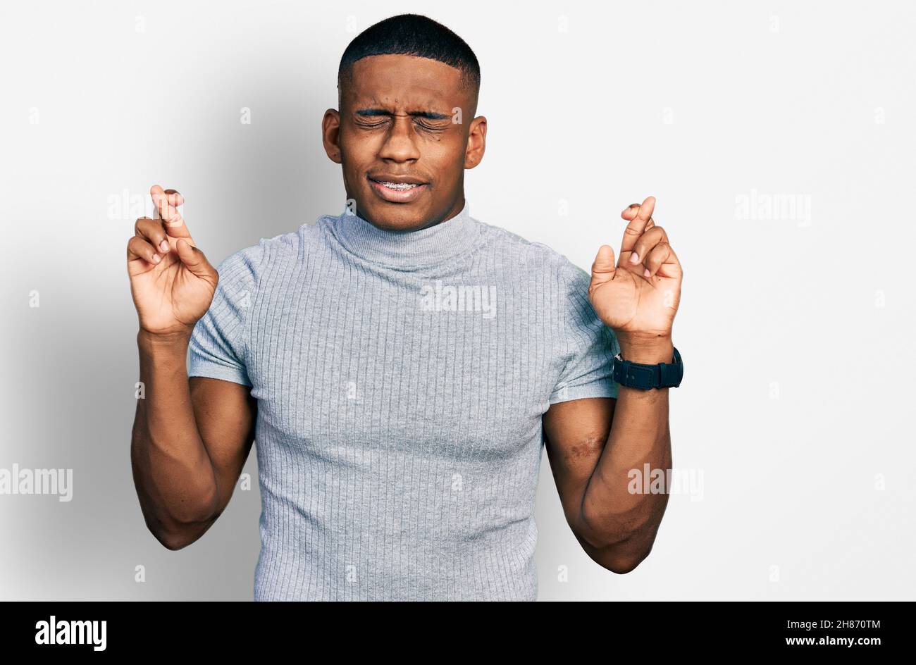 Young black man wearing casual t shirt gesturing finger crossed smiling ...