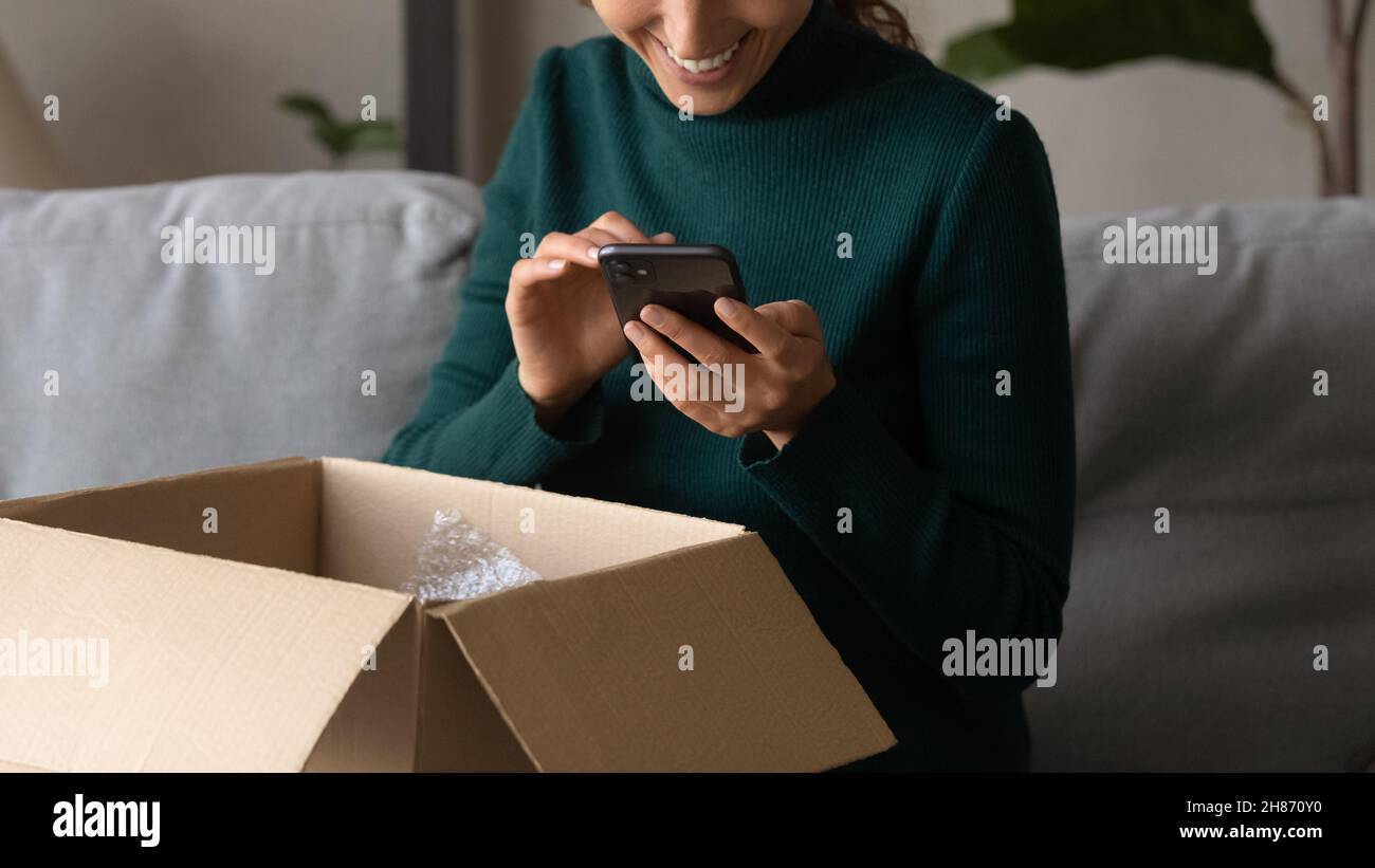 Smiling millennial female order consumer products delivery online using phone Stock Photo