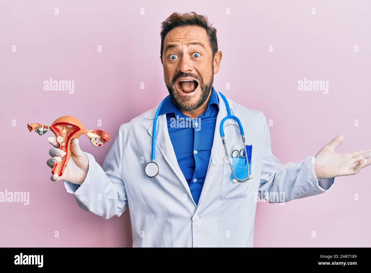 Middle age gynecologist man holding anatomical model of female genital organ celebrating achievement with happy smile and winner expression with raise Stock Photo