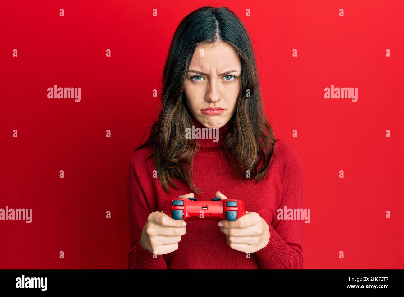 Young brunette woman playing video game holding controller skeptic and ...