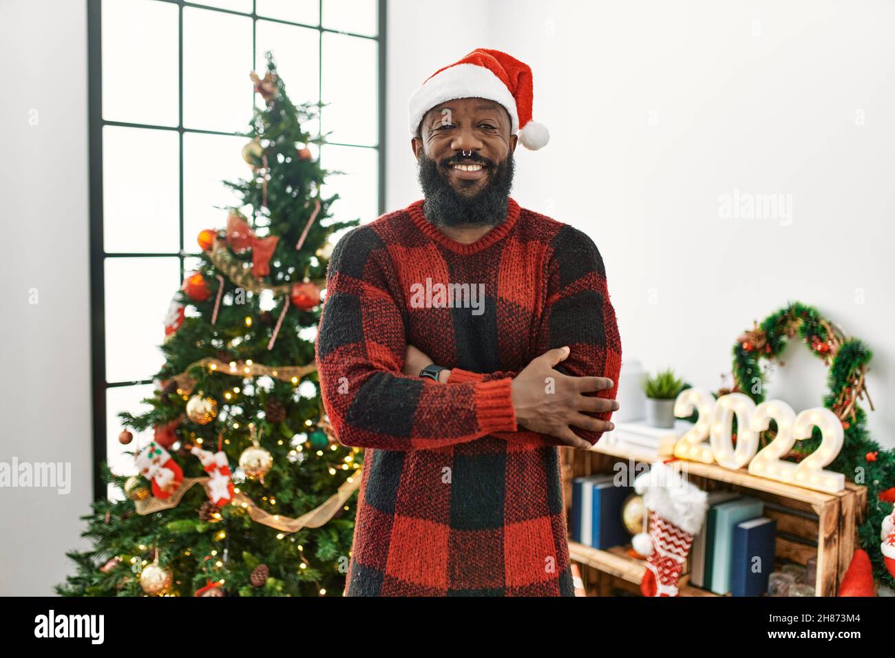 African american man wearing santa claus hat standing by christmas tree ...