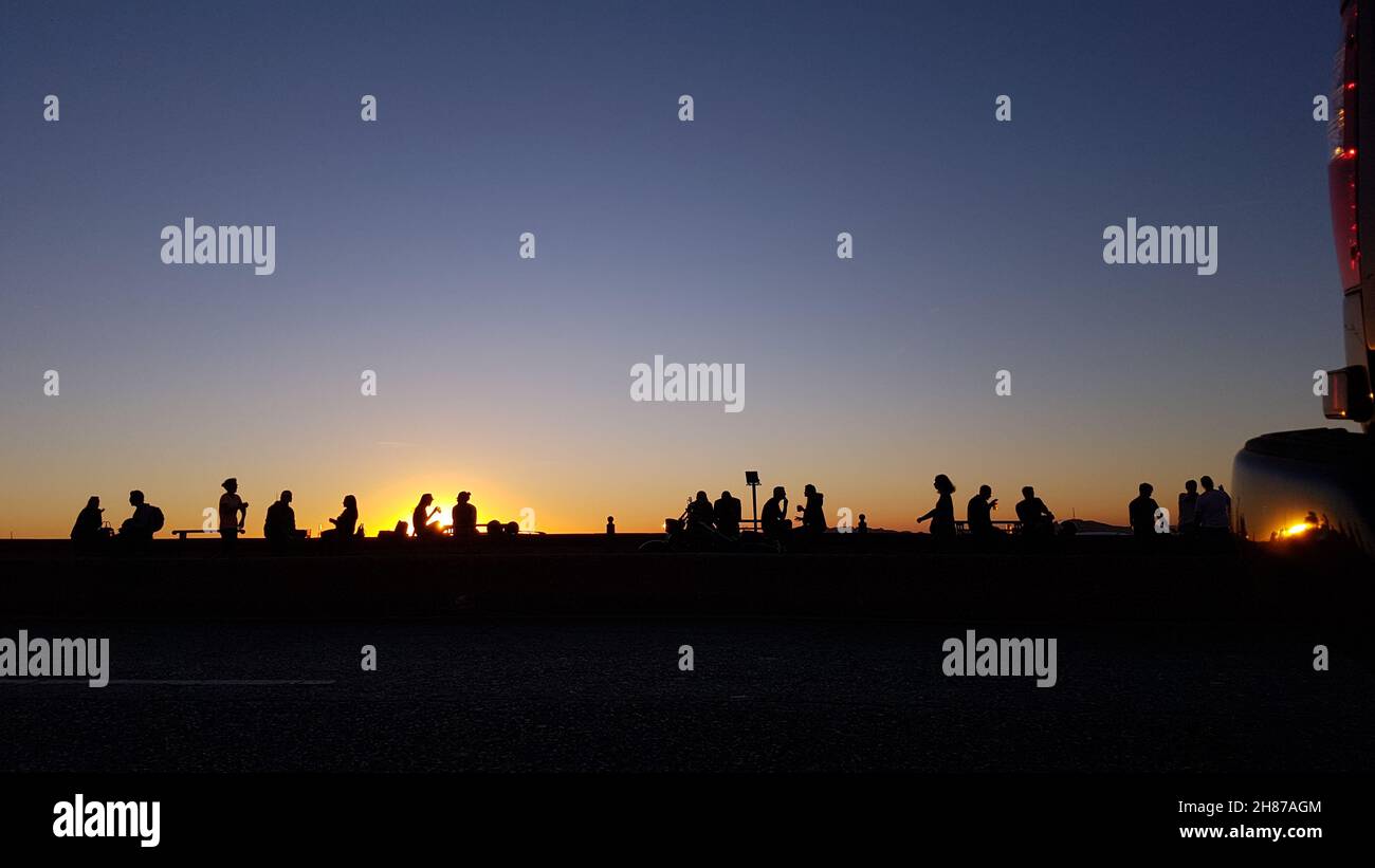 Ombres chinoise et contre jour d'amis se retrouvant pour boire un verre en extérieur sur un petit muret. Taking a drink with friends outdoor. sunset Stock Photo