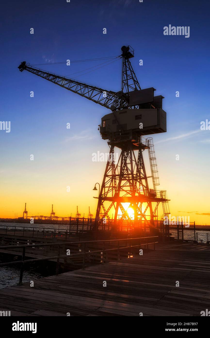 Cargo crane in Port Phillip bay docks at sunset against dark sky and orange sun. Stock Photo