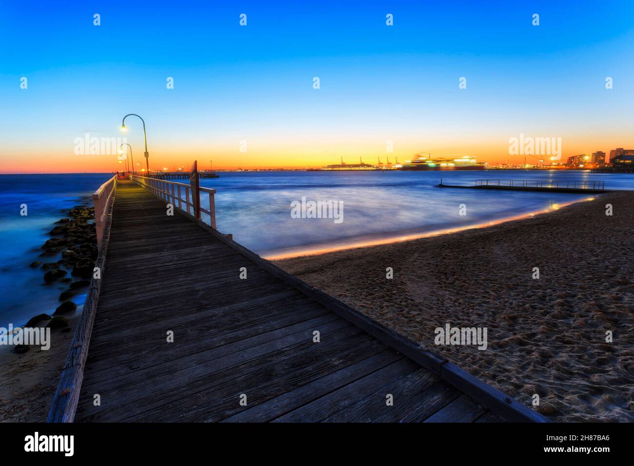Port Phillip bay wooden jetty on sandy beach at sunset in Melbourne, Australia - view towards departing ferry. Stock Photo