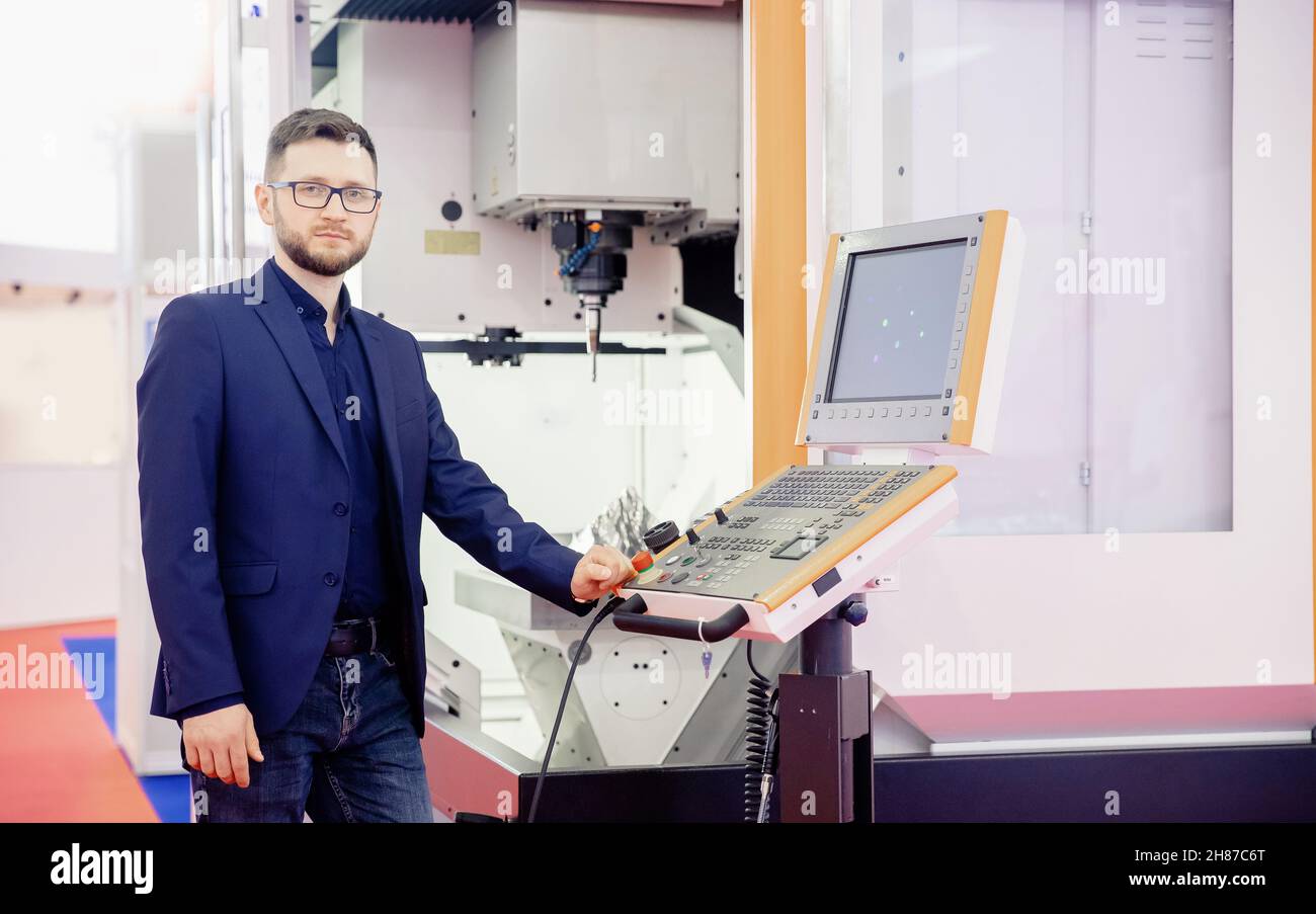 Engineer young man in glasses operates CNC automatic metalworking lathe or laser, industrial worker in modern factory. Stock Photo