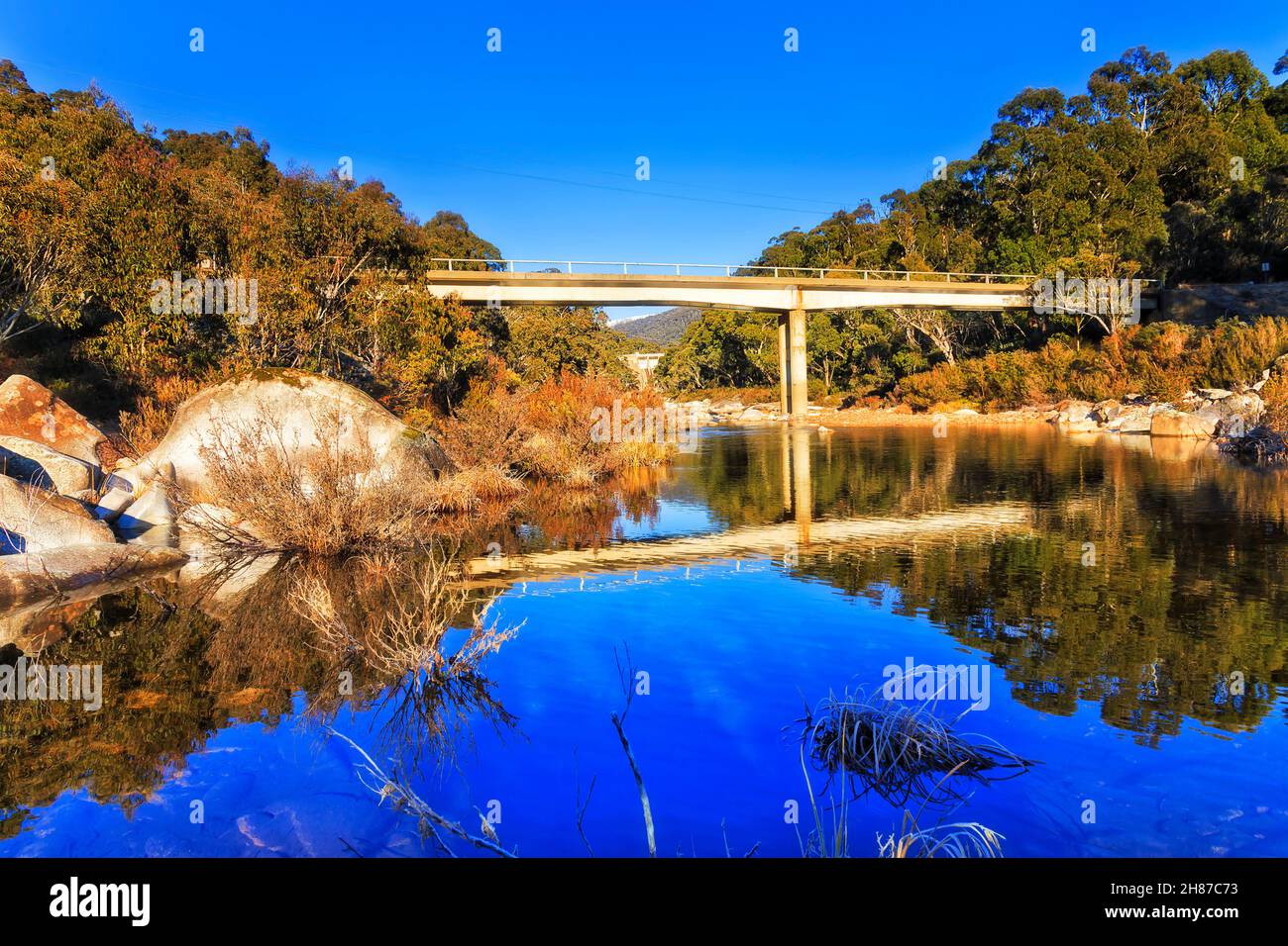 Snowy river under Guthega Bridge in Snowy mountains of Australia on a sunny winter day with frost on still water bay. Stock Photo