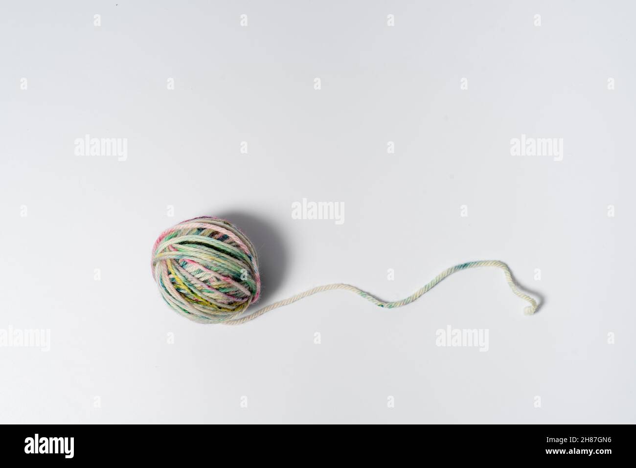 Small ball of light multicolored yarn with a loose string on white ...