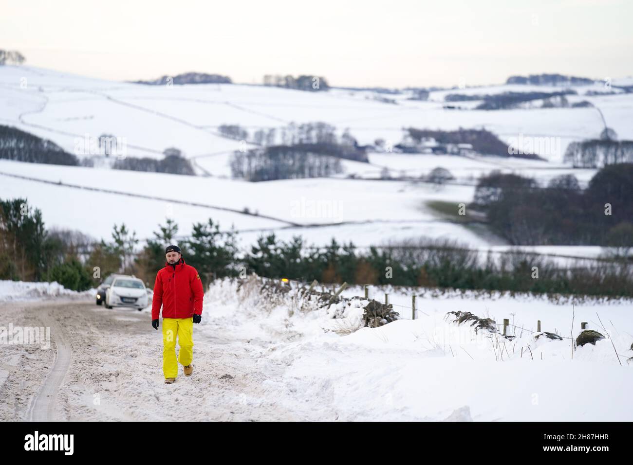 A motorist walks along the snow-covered A515 near Biggin, in the Peak District, Derbyshire, amid freezing conditions in the aftermath of Storm Arwen. Picture date: Sunday November 28, 2021. Stock Photo