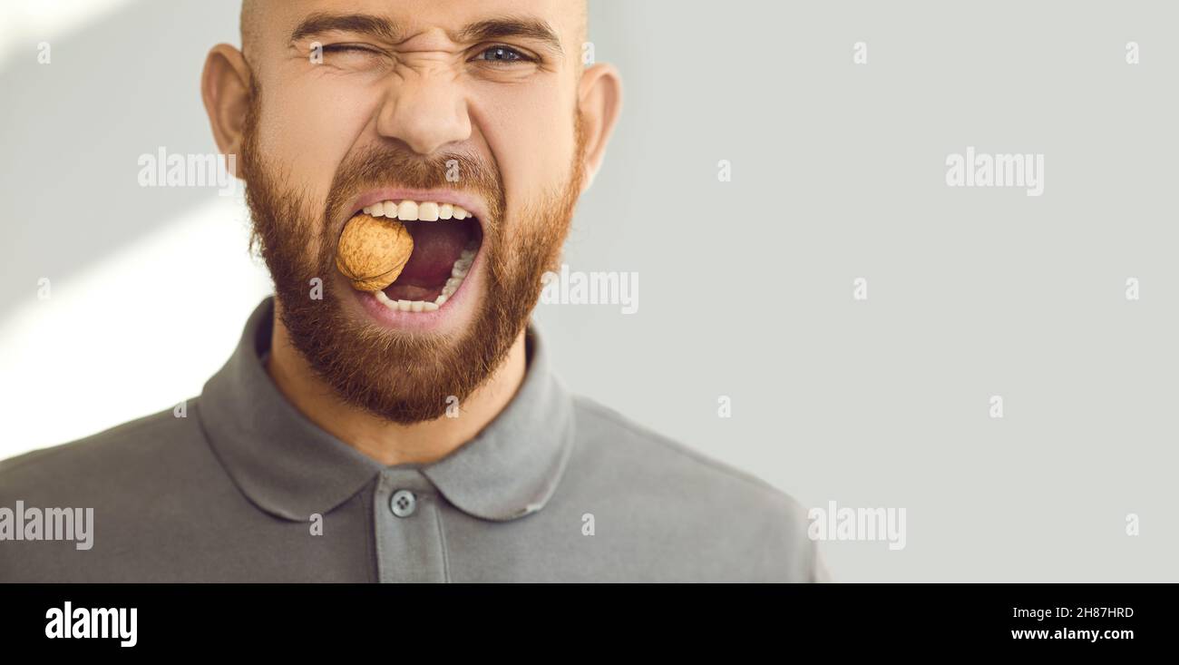 Headshot portrait of a young man with healthy teeth trying to crack a hard walnut Stock Photo