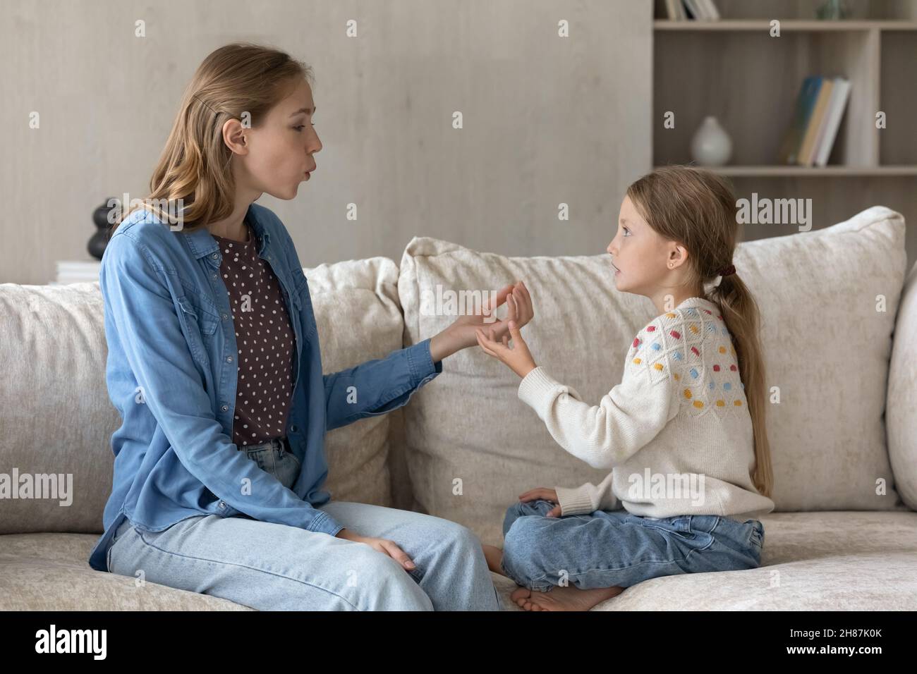 Focused caring young mother teaching little kid daughter pronouncing sounds. Stock Photo