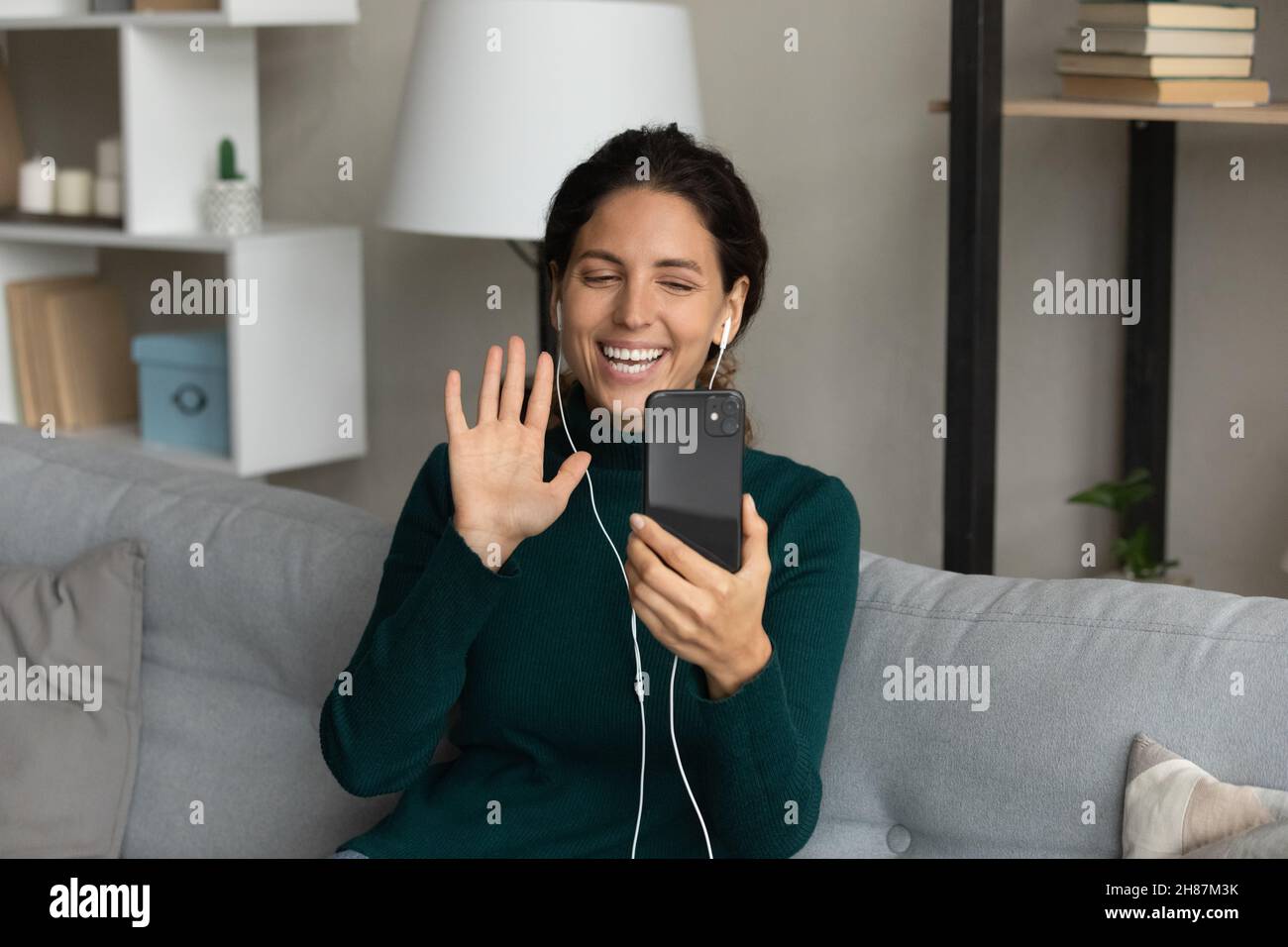 Cheerful hispanic woman wear headphones wave hand to phone webcam Stock Photo