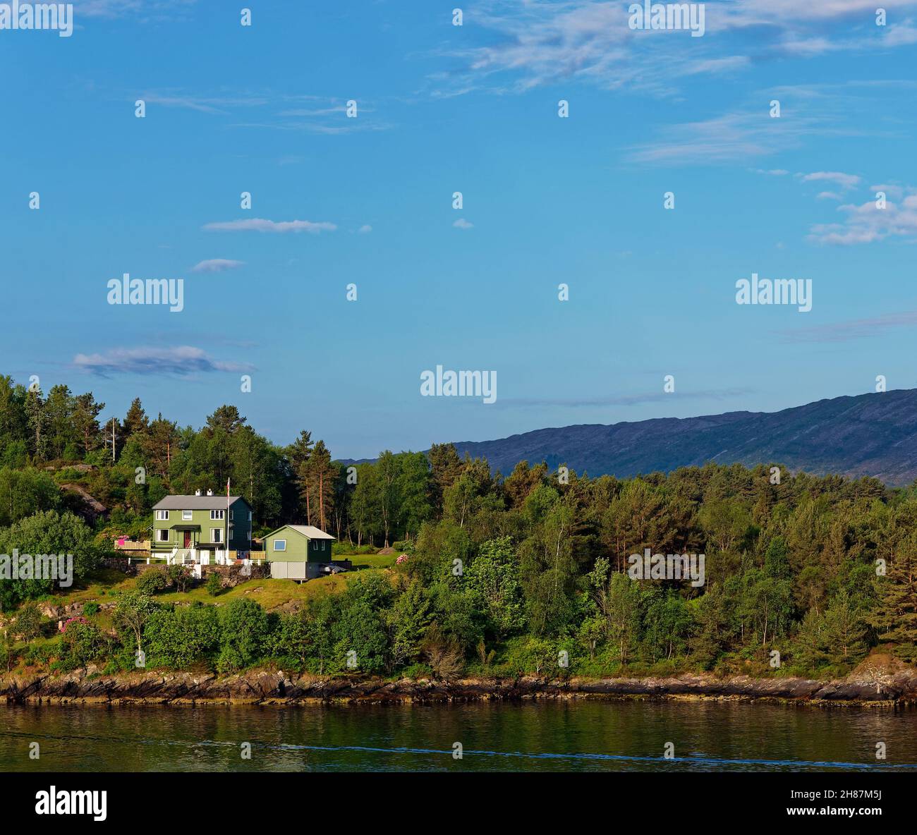 A Traditional Green Painted Wooden House set amongst the Pines of a small Island in Bergen fjord on a sunny Summers morning in July. Stock Photo