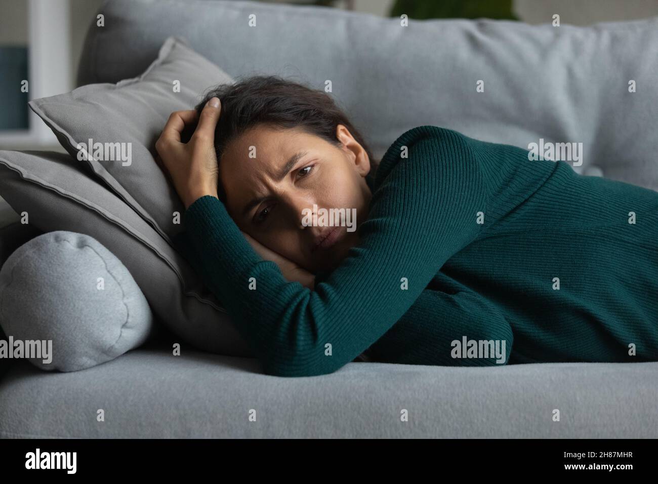 Depressed millennial latina female lie on sofa without sleep Stock Photo