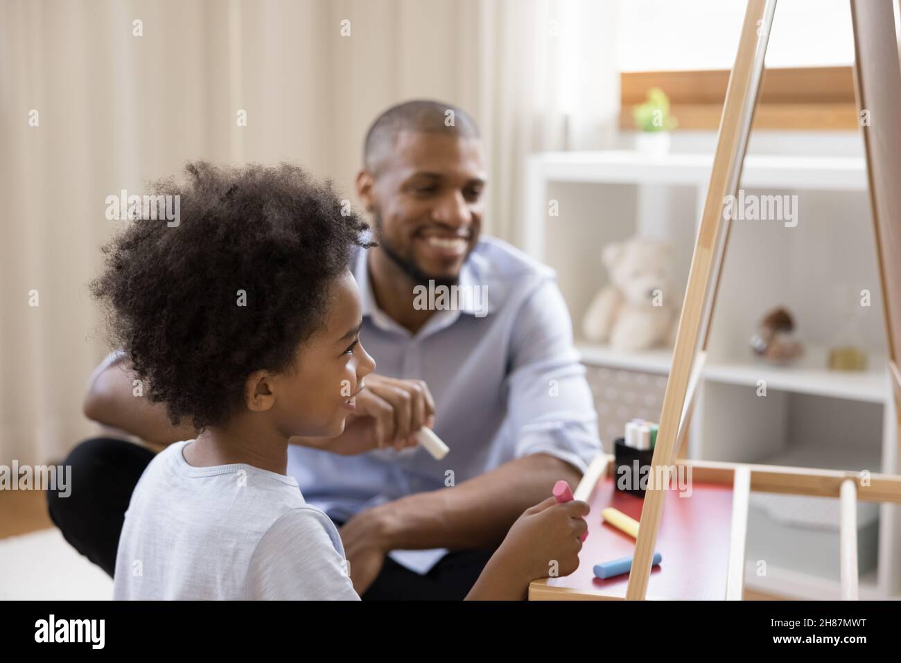 Happy cute Black little kid and dad drawing on chalkboard Stock Photo