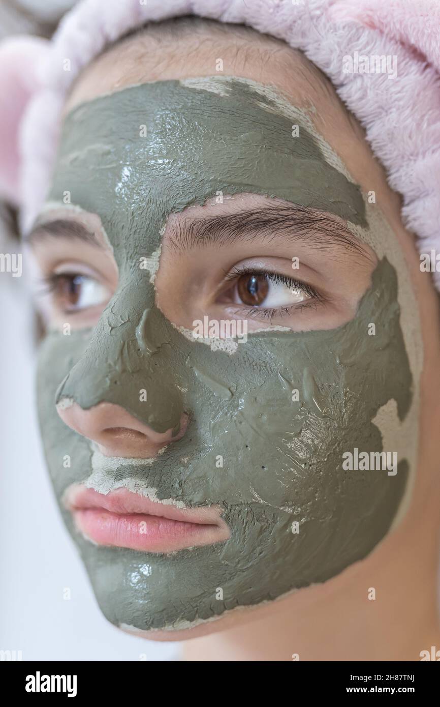 teenage girl of attractive appearance with brown eyes with mask of gray clay on her face in profile . female takes care of skin at home during isolati Stock Photo