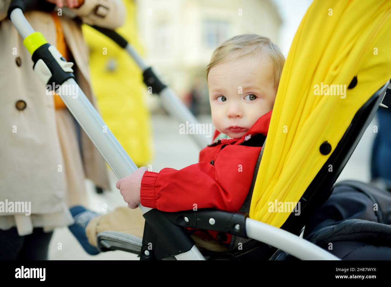 Sweet baby boy wearing red jacket sitting in a stroller outdoors