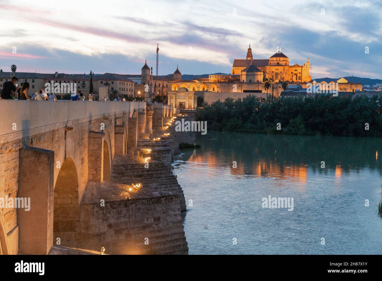 View of the Roman Bridge of Cordoba and the Mosque in the background with people walking in the blue hour of the day Stock Photo