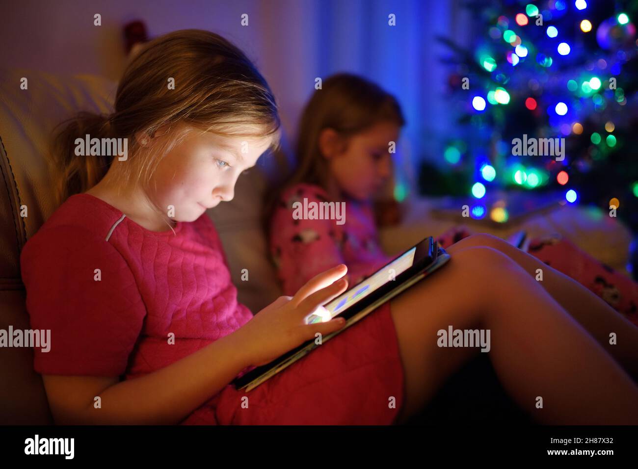 Two adorable little sisters playing with a digital tablet in a dark ...