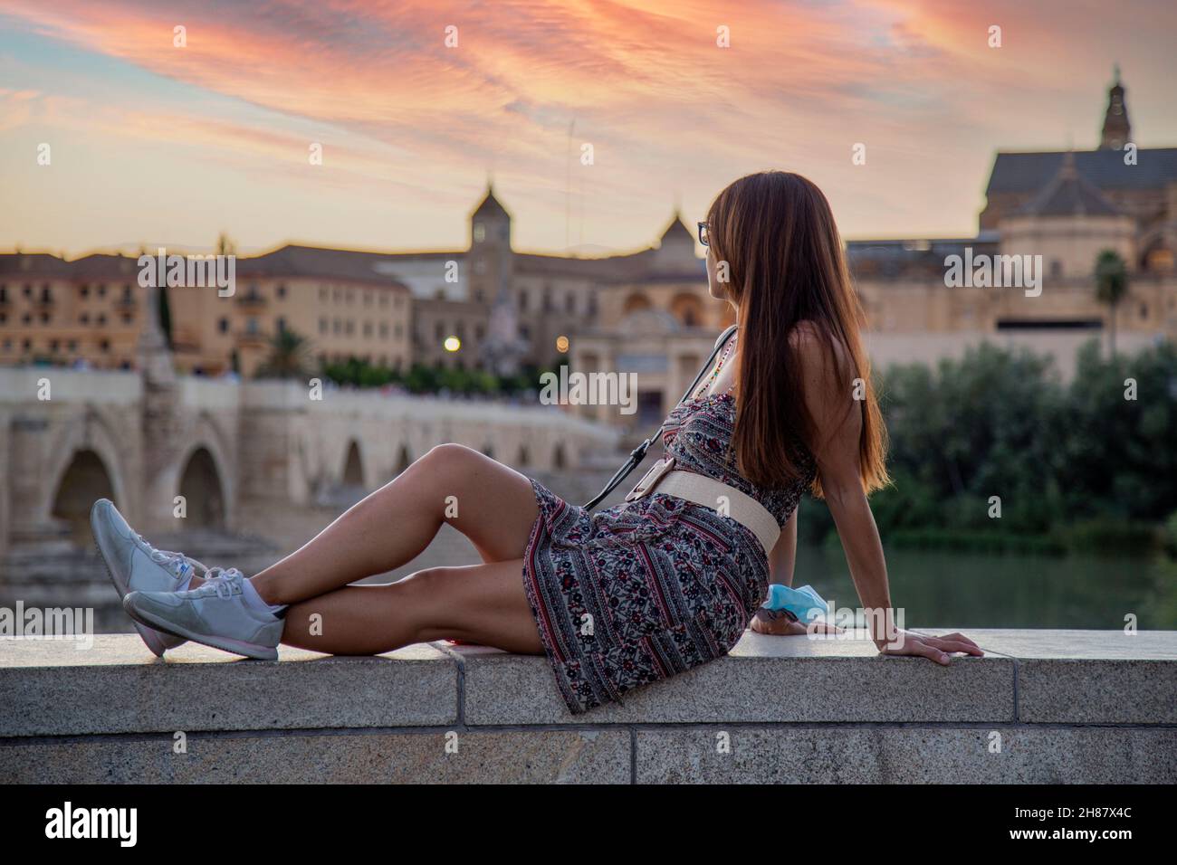 Brunette girl with long hair and summer dress looking at sunset at the Roman Bridge of Cordoba Stock Photo