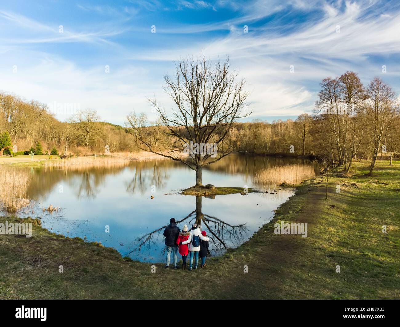 Aerial view of family of four having fun by a lake or pond on sunny spring day. Family having quality time together outdoors. Exploring nature with ki Stock Photo