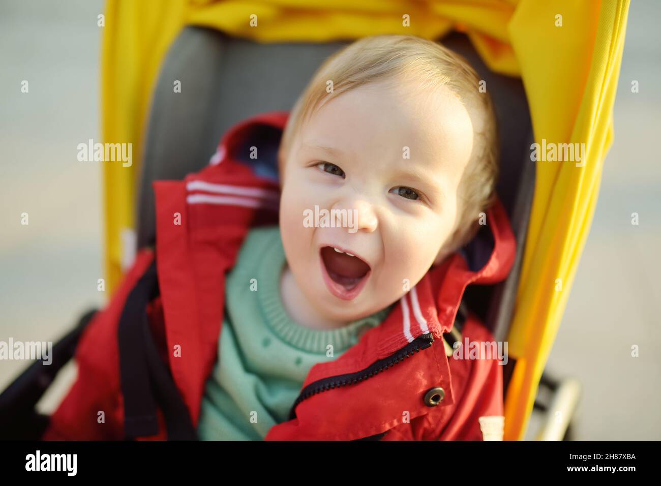 Sweet baby boy wearing red jacket sitting in a stroller outdoors