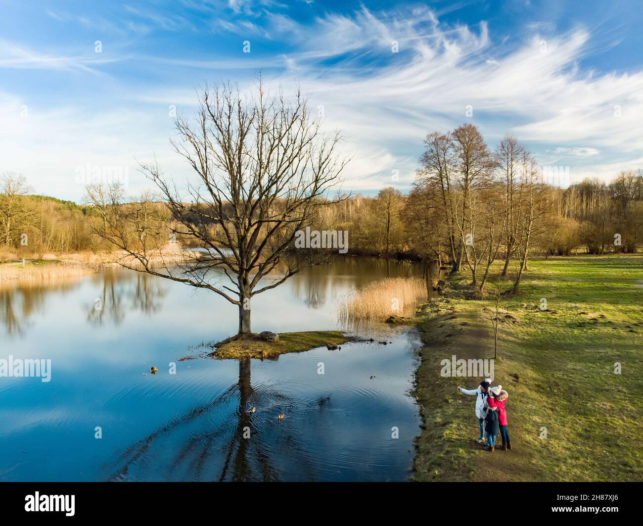 Aerial view of Mother and her kids having fun by a lake or pond on sunny spring day. Family having quality time together outdoors. Exploring nature wi Stock Photo