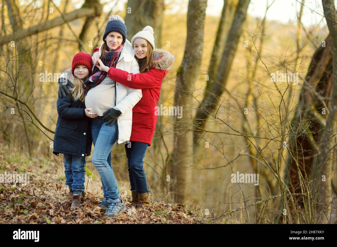 Young pregnant woman hugging her older daughters. Older siblings having fun with her pregnant mom outdoors. Mother and her kids spending quality time Stock Photo