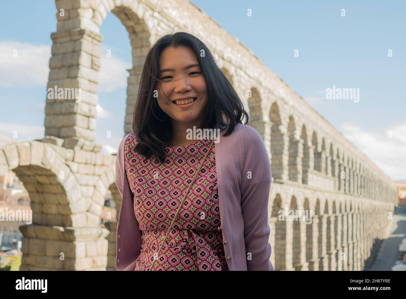 Attractive Asian girl during vacation in Spain - young happy and beautiful Japanese woman visiting world heritage aqueduct in Segovia enjoying holiday Stock Photo