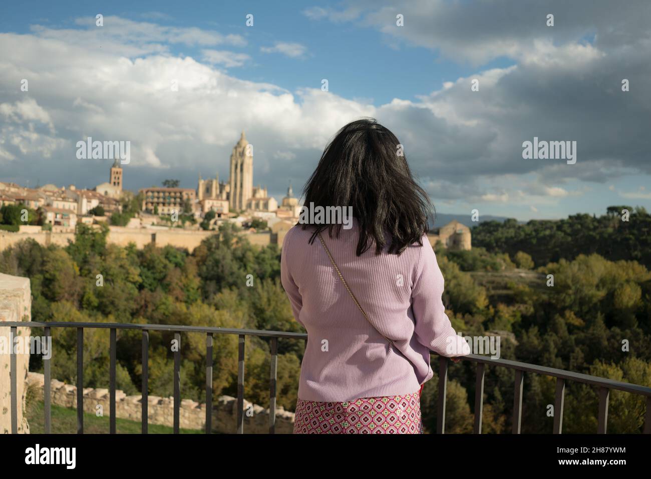 back view of young happy and relaxed woman enjoying old town and forest panoramic view from viewpoint during holiday travel in Europe Stock Photo