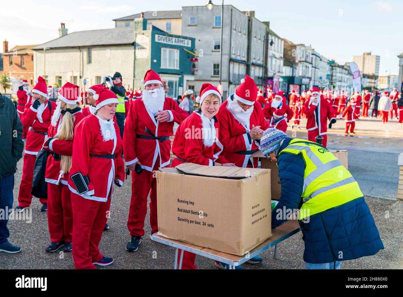 Lines of people, all dressed as Father Christmas, queuing up to register for a place in the 'Santa's on the Bay' charity fun run in aid of the Pilgrims hospices on the seafront at Herne Bay in Kent on a bitterly cold morning in late November. Stock Photo