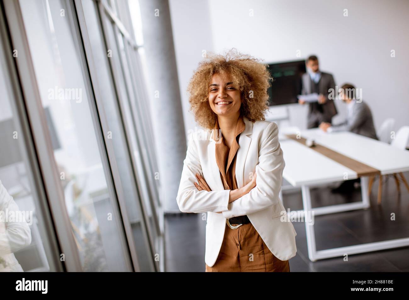 Young curly hair businesswoman standing in the office with young people works behind her Stock Photo