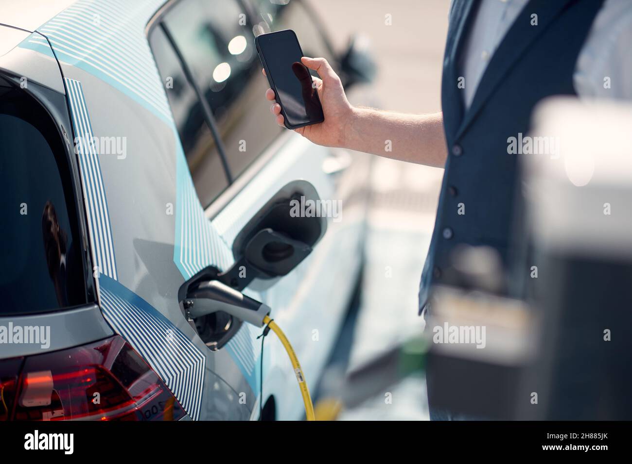 A young man is waiting for his electric car to charge at the station on