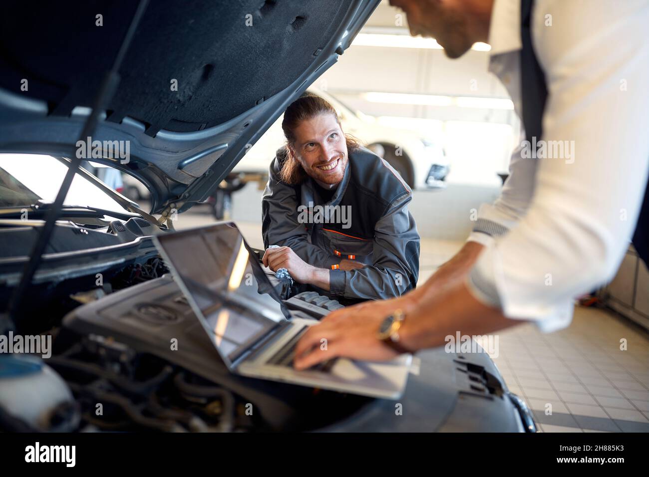 Smiling mechanic repairs auto.diagnostics on laptop. Stock Photo