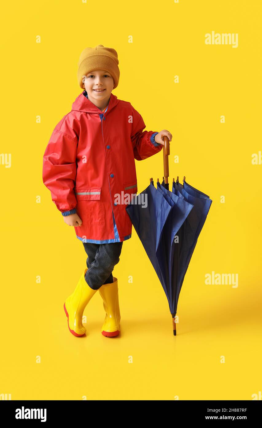 Little boy in raincoat and with umbrella on color background Stock