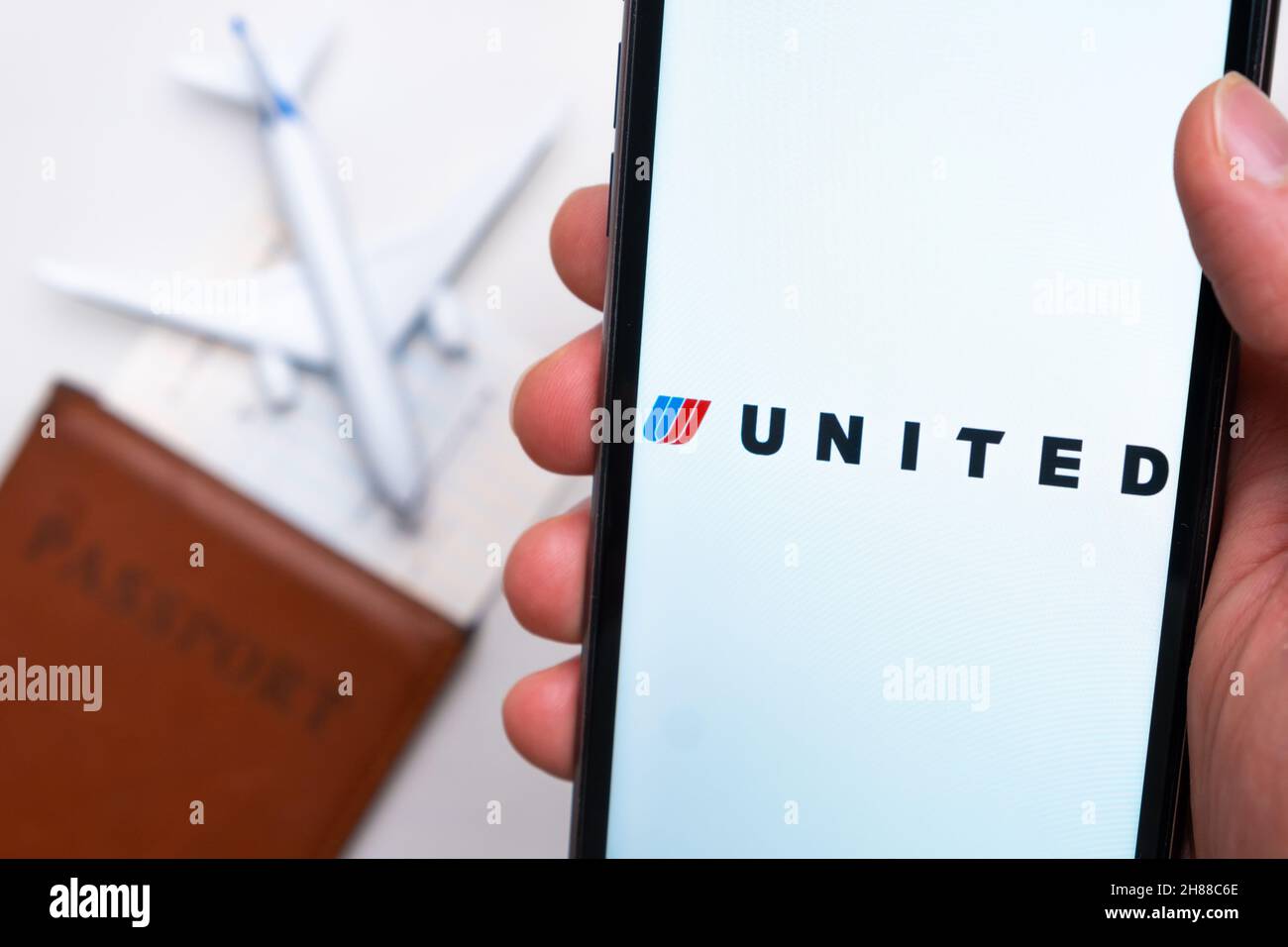 United Airlines app on the cell phone screen in mans hand with plane, boarding pass and passport