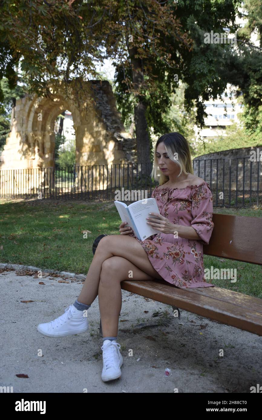 woman reading a book in a park during sunny day looking camera,looking book,sitting on a bench, during a winter, summer day Stock Photo