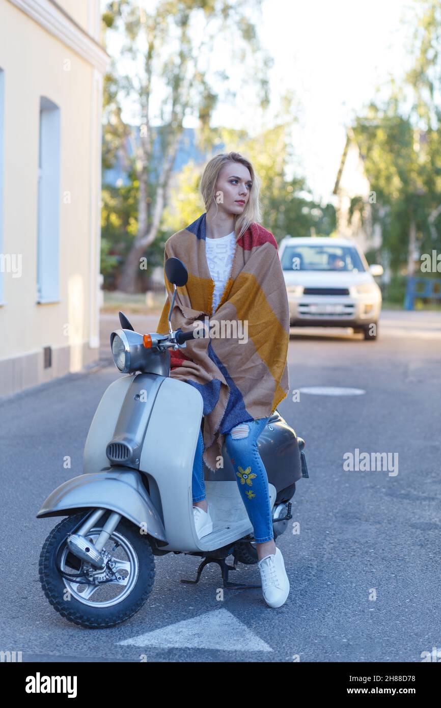 Attractive girl's portrait. Lady in jeans, short t-shirt and straw hat sitting on a retro moped in a city. Travel concept. Stock Photo