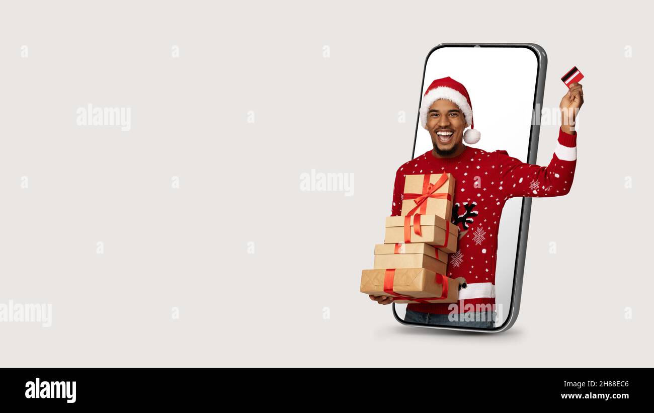 Happy black guy in Santa hat posing inside huge cellphone Stock Photo