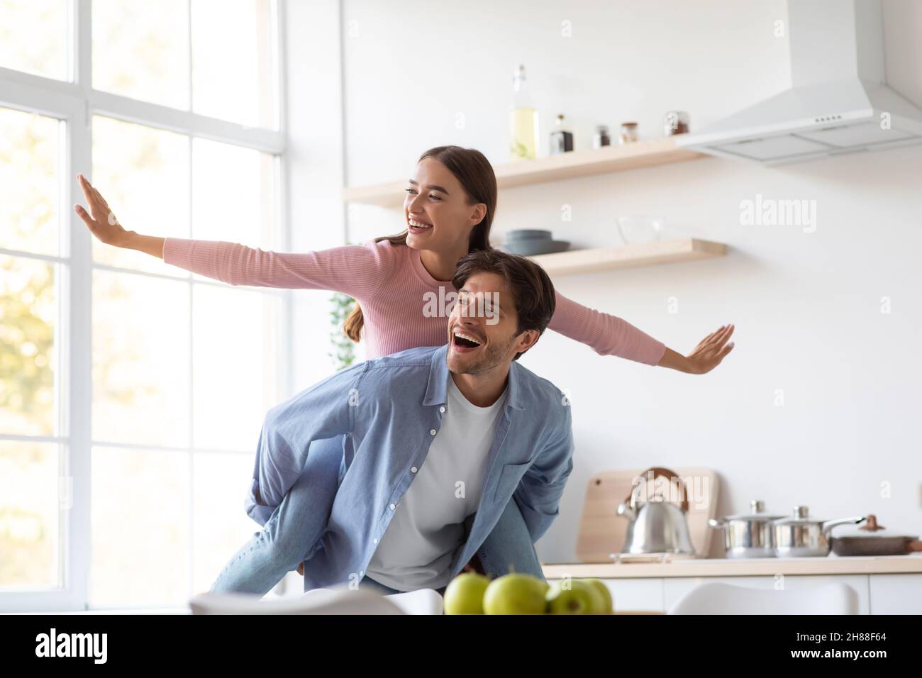 Cheerful excited positive caucasian young man with woman riding his back with arms to sides Stock Photo