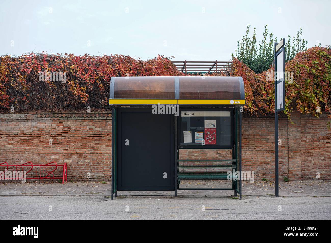 Bus stop in front of a wall and bushes. To the left, a red bicycle stand. Stock Photo
