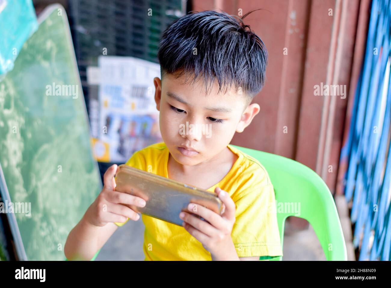 Asian child with squint eyes playing mobile game with smartphone. Concept of eye strain, screen addiction and excessive screen time. Stock Photo